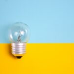 A clear light bulb against a vibrant blue and yellow background, symbolizing energy and creativity.
